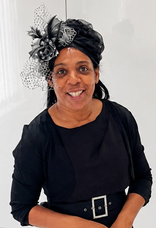 Vivean, the founder of Brynels British Millinery, wearing a black outfit with a decorative headpiece against a white background